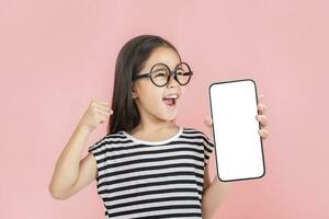 ásia pequeno menina segurando Smartphone brincar do em branco tela e sorridente em branco fundo. foto