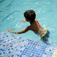 feliz indiano Garoto natação dentro uma piscina, criança vestindo natação traje ao longo com ar tubo durante quente verão Férias, crianças Garoto dentro grande natação piscina. foto