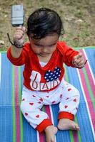 fofa pequeno indiano infantil sentado desfrutando ao ar livre tiro às sociedade parque dentro Délhi, fofa bebê Garoto sentado em colorida esteira com Relva em volta, bebê Garoto ao ar livre tiro foto