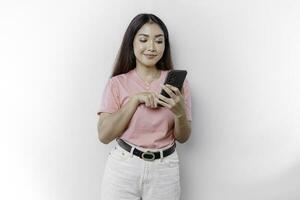 uma retrato do uma feliz ásia mulher é vestindo Rosa camiseta e segurando dela telefone, isolado de branco fundo foto