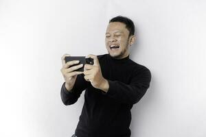 jovem ásia homem dentro casual vestem é jogando jogos com Móvel telefone com uma branco fundo isolado. foto