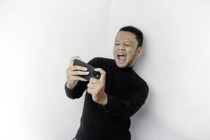 jovem ásia homem dentro casual vestem é jogando jogos com Móvel telefone com uma branco fundo isolado. foto