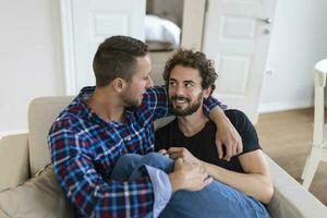 alegre jovem gay casal sentado junto. dois afetuoso masculino amantes sorridente alegremente enquanto abraçando cada outro. jovem gay cupê ser romântico. foto