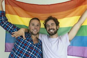 dois jovem gay amantes olhando às cada de outros carinhosamente. dois jovem masculino amantes em pé juntos contra uma orgulho bandeira. afetuoso jovem gay casal partilha uma romântico momento junto. foto