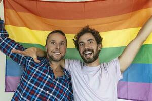 dois jovem gay amantes olhando às cada de outros carinhosamente. dois jovem masculino amantes em pé juntos contra uma orgulho bandeira. afetuoso jovem gay casal partilha uma romântico momento junto. foto