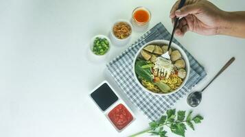 almôndega, dentro Indonésia conhecido Como Bakso ou baso. servido com Macarrão legumes Pimenta molho dentro uma tigela em branco fundo com mão. fechar acima topo Visão plano deitar foto