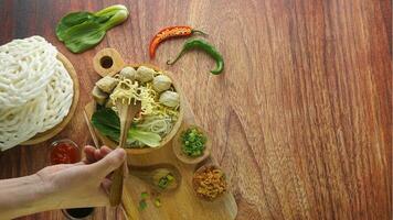 almôndega, dentro Indonésia conhecido Como Bakso ou baso. servido com Macarrão legumes Pimenta molho dentro uma tigela em madeira fundo com mão. fechar acima topo Visão plano deitar cópia de espaço foto