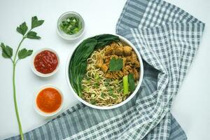 Macarrão com frango, dentro Indonésia isto é conhecido Como mie ayam. servido com verde vegetal Pimenta molho dentro uma tigela em branco de madeira fundo de mão foto