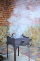 churrasco grade com flamejante carvão e fumaça, dentro a quintal contra vermelho parede tijolos fundo. conceito do verão piquenique foto