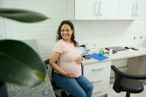 retrato do uma feliz grávida mulher sorridente uma segurando dela barriga, visitando médico clínica para gravidez checar foto