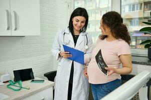 sorridente grávida mulher visitando médico ginecologista obstetra dentro ginecológico clínica, durante regular médico checar foto
