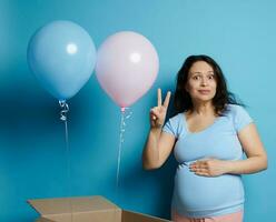 espantado grávida mulher esperando gêmeos, posando com Rosa e azul balões a partir de uma caixa durante bebê chuveiro ou gênero festa foto