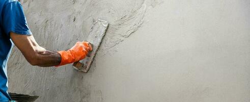 mão fechada do trabalhador rebocando cimento na parede para construir casa foto