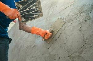 mão fechada do trabalhador rebocando cimento na parede para construir casa foto