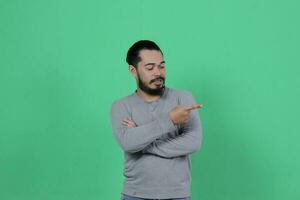 barbudo ásia homem poses vestindo uma cinzento camisa contra uma verde fundo foto