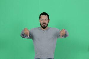 barbudo ásia homem poses vestindo uma cinzento camisa contra uma verde fundo foto