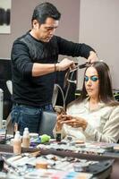 estilista usando plano ferro em cabelo do fêmea cliente sentado dentro salão cadeira foto