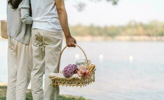 casal caminhando dentro jardim com piquenique cesta. dentro amor casal é desfrutando piquenique Tempo dentro parque ao ar livre foto