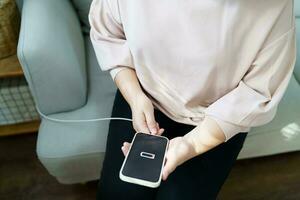 mulher mãos cobrando Móvel telefone bateria com baixo bateria. obstrução uma carregador dentro uma inteligente telefone com energia banco banco de poder poder carregador moderno estilo de vida energia tecnologia conceito foto