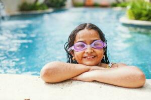fofa indiano pequeno menina natação dentro uma piscina, posando, olhando às Câmera foto