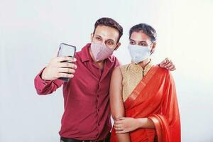indiano homem levando selfie juntos com dele namorada ou esposa enquanto vestindo uma coronavírus proteção mascarar foto