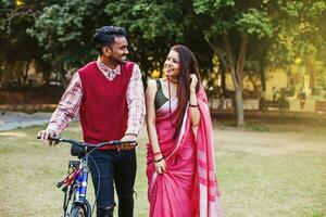 jovem indiano casal dentro tradicional étnico roupas caminhando com a bicicleta dentro a parque foto