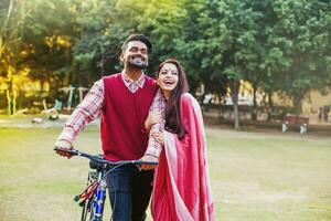 jovem indiano casal dentro tradicional étnico roupas caminhando com a bicicleta dentro a parque foto