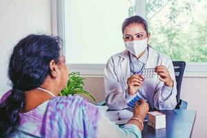 indiano médico dentro uma mascarar dando pílulas para a idosos mulher foto