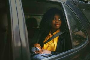 lindo africano americano mulher segurando uma bebê dentro uma carro costas assento foto