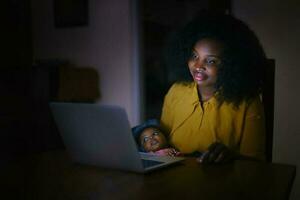 mãe sentado às noite com a bebê dentro frente do a computador portátil foto