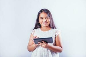 fofa indiano pequeno menina usando tábua computador em dela estúdio retrato em branco fundo foto