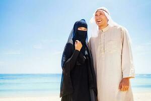 muçulmano casal em uma de praia vestindo tradicional vestir foto