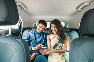 jovem indiano casal vestindo tradicional étnico roupas usando Móvel telefone em uma costas assento do uma carro foto