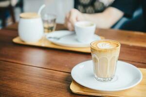 uma vidro copo do flautim café com leite em de madeira mesa dentro a café fazer compras. foto