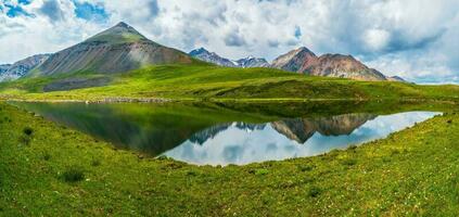 brilhante verde azul alpino panorama com montanha lago dentro terras altas vale dentro luz solar e grande montanha debaixo azul nublado céu. sombra do nuvens em verde montanha vale. panorâmico Visualizações. foto