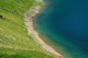 uma íngreme verde montanha declive acima uma turquesa Claro montanha lago. natural ecológico fundo. foto