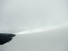 minimalista cenário com pequeno homem em ampla Nevado montanha dentro luz solar debaixo nublado céu. atmosférico panorama com brilho do sol em Alto neve montanha às mutável clima. névoa montanha dentro nublado. foto