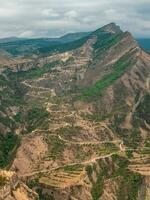 vertical Visão do uma montanha vale com uma serpentina estrada. perigoso limitar sujeira montanha estrada através a colinas para uma grande altitude Vila. foto