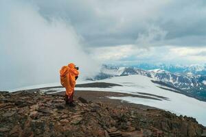 extremo expedição para a montanhas. uma viagem fotógrafo leva uma cenário em pé às a topo do uma lindo Visão dentro a Alto Nevado montanhas. viajando trabalhador autonomo, ao ar livre aventura viagem conceito. foto