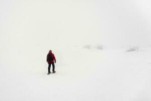 polar expedição. uma solitário viajante em sapatos de neve anda em ao longo uma Nevado declive dentro uma nebuloso gelado mortalha. forte norte clima, pobre visibilidade. foto