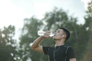 jovem homem bebendo água depois de trabalhando Fora exercício às a parque. foto
