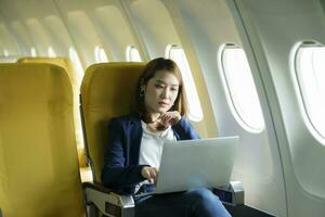 o negócio mulher trabalhando em computador portátil enquanto sentado dentro avião. foto