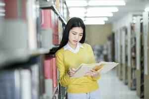 aluna em pé e lendo livro às biblioteca. foto