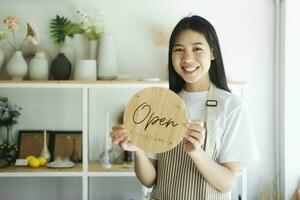 jovem ásia o negócio proprietário girando aberto placa produtos loja e pronto para serviço para bem-vinda a cliente. foto