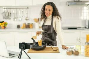 mulher latina gravando vídeo e cozinhando na cozinha foto