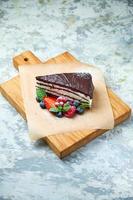 uma fatia de bolo de chocolate decorado com frutas vermelhas em uma placa de madeira foto