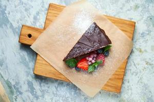 uma fatia de bolo de chocolate decorado com frutas vermelhas em uma placa de madeira foto