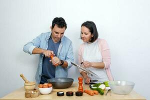 jovem casal cozinhando em uma mesa cheio do ingredientes em uma branco fundo foto