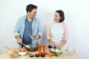 uma sorridente casal cozinhando às uma mesa em uma branco fundo foto