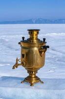 uma samovar carrinhos em uma peça do gelo em uma embaçado fundo do uma lago dentro a neve e montanhas dentro a distância. uma cobre russo a lenha chaleira. russo hospitalidade. cópia de espaço. vertical. foto